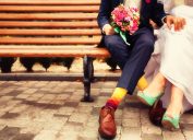 Chest-down view of a bride and groom on a bench wearing colorful shoes and socks