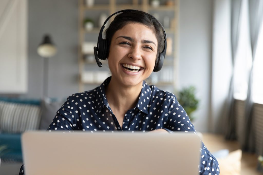 Woman sitting at a laptop laughing and wearing a headset
