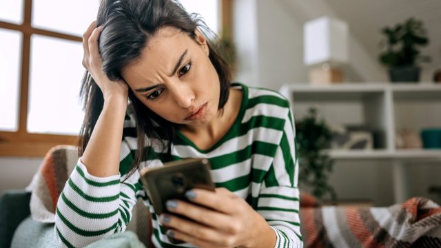 Frustrated woman using mobile phone while sitting on sofa