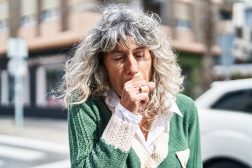 Middle aged woman coughing in the street