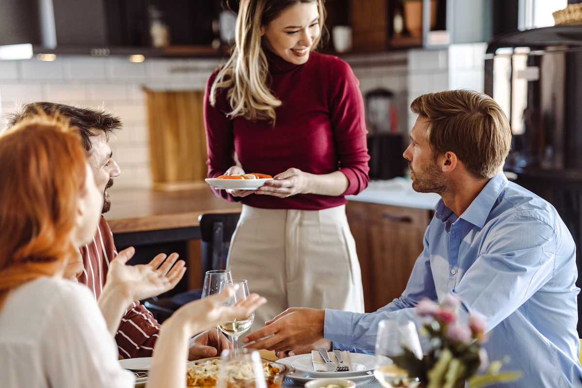 Woman is serving her friends at the dining room table during a dinner party.