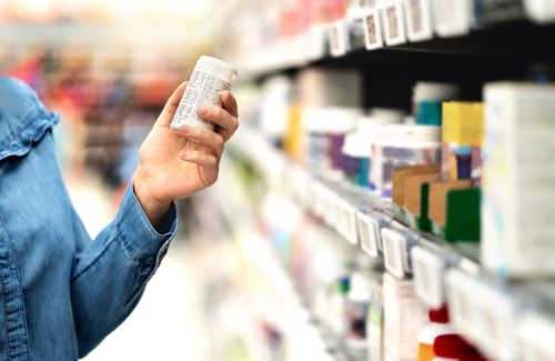 Customer in pharmacy holding medicine bottle. Woman reading the label text about medical information or side effects in drug store. Patient shopping pills for migraine or flu. Vitamin or zinc tablets.
