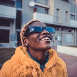 A person wearing an orange coat and protective solar glasses looking up into the sky with a smile