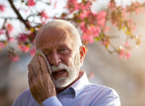 Senior man wiping eyes with tissue outdoors