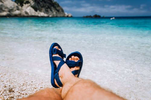 Young male crossed feets in blue flip-flop sandal sunbathing on sea beach