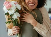 Portrait of two women hugging each other and holding flowers.