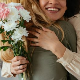Portrait of two women hugging each other and holding flowers.