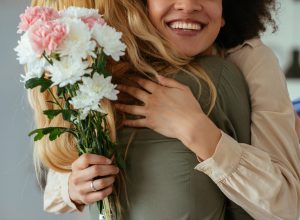 Portrait of two women hugging each other and holding flowers.