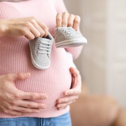 pregnant woman holding tiny shoes near her belly while husband hugs her