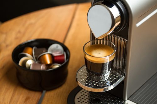 Nespresso coffee machine on a wood counter with a bowl of coffee pods