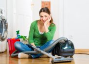 Young woman cleaning at home, she has a cleaning day and using a vacuum cleaner cleaning products and a bucket but she does not feel like it