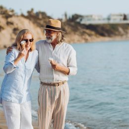 Happy mature couple walking by the sea, eating ice cream