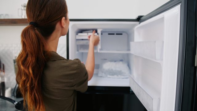 Rear view of a young brunette woman putting something in the freezer