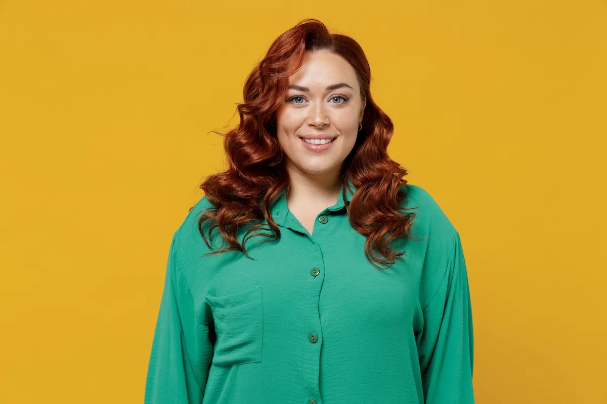Amazing bright happy young ginger chubby overweight woman 20s years old wears green shirt looking camera smiling isolated on plain yellow background studio portrait. People emotions lifestyle concept