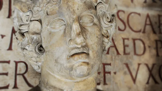 Close up of classical Roman statue against Latin inscription