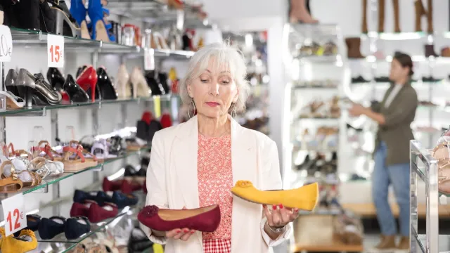 Senior woman standing in a shoe store examining two pairs of flats