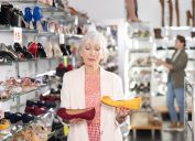 Người phụ nữ lớn tuổi đứng trong một cửa hàng giày kiểm tra hai đôi giày bệt