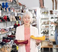 Senior woman standing in a shoe store examining two pairs of flats