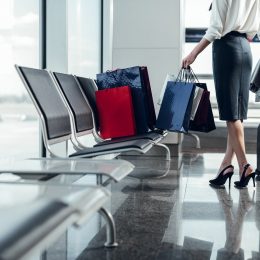 A person standing in the airport with shopping bags and their luggage