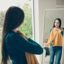 Young woman trying on yellow sweater in mirror