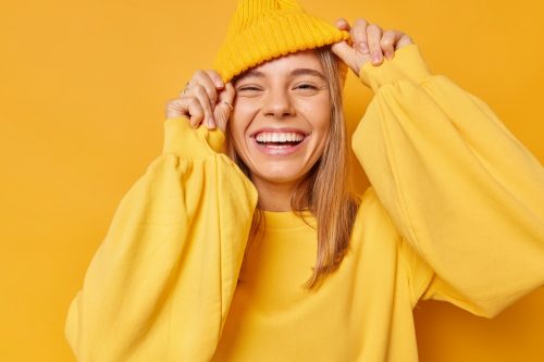 Người phụ nữ trẻ mỉm cười hạnh phúc trong chiếc váy màu vàng và chiếc mũ len