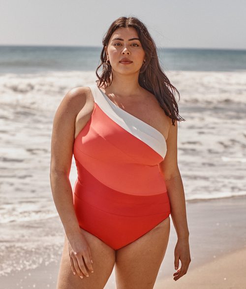 Model on the beach in Summersalt's coral Sidestroke swimsuit