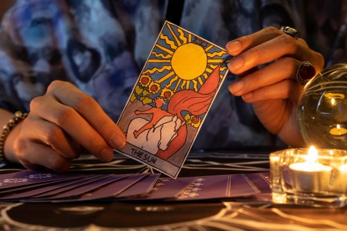 Tarot card reader holding THE SUN card and tarot cards on table near burning candles in candle light