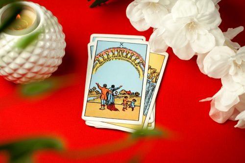 Ten of Cups tarot card on red background with white flowers next to it