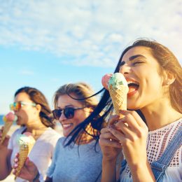 Three young woman eating ice cream cones at the seaside as they stroll along a waterfront promenade