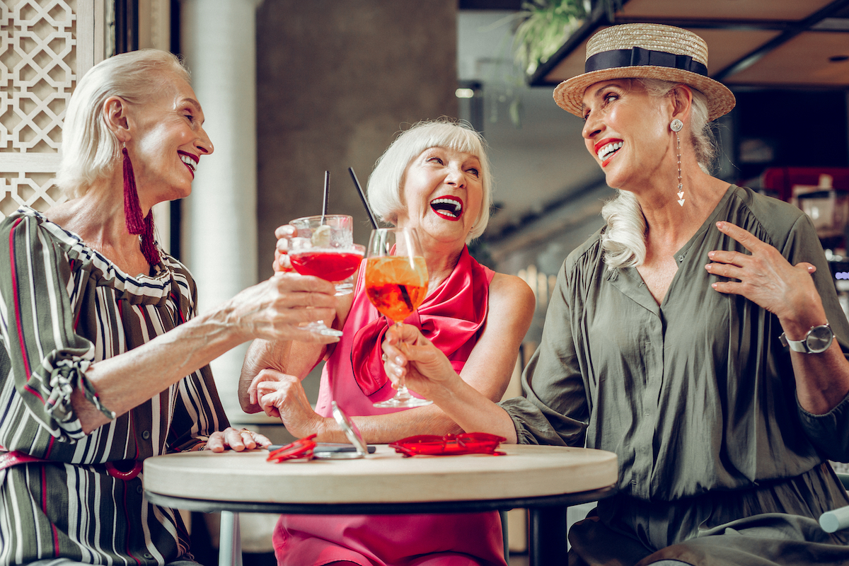 Three stylish senior women laughing and having drinks