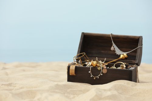 Open wooden chest with treasures on sandy beach