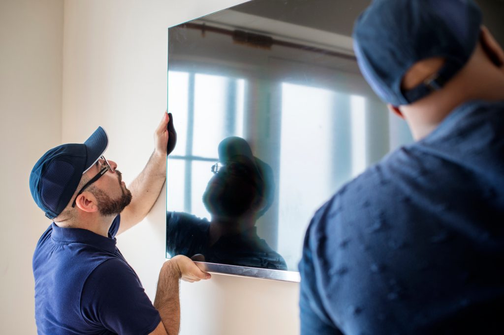 Two delivery people installing a television on the wall