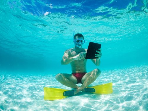 Young man sitting underwater checking his social media on a waterproof tablet