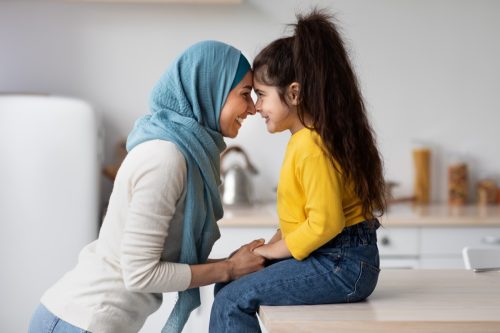 little girl bonding with her Muslim mother in kitchen.