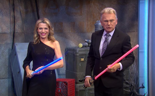 Vanna White and Pat Sajak holding lightsabers