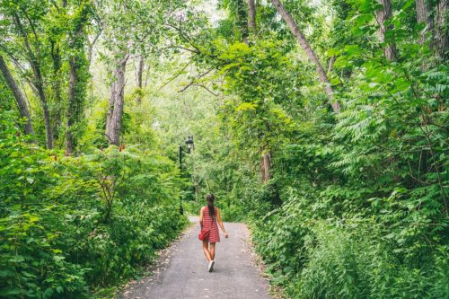 Woman in red dress walking in woods trail path.