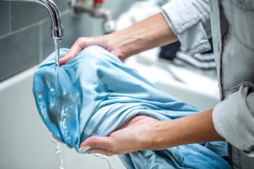 người phụ nữ làm sạch áo sơ mi bị ố trong bồn rửa trong phòng tắm.