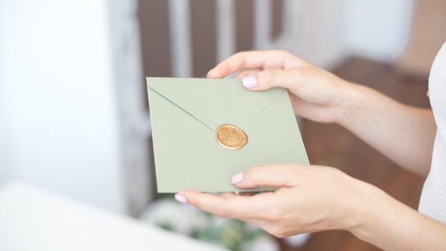 Close up photo of female hands holding invitation envelope with a wax seal, a gift certificate, a postcard, wedding invitation card.