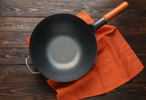 Empty iron wok with napkin on wooden table, top view