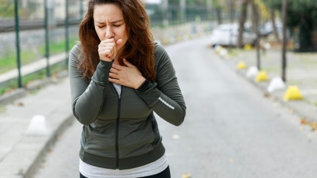 Young sporty woman coughing while walking on the street. Athlete woman affected by air pollution during running training