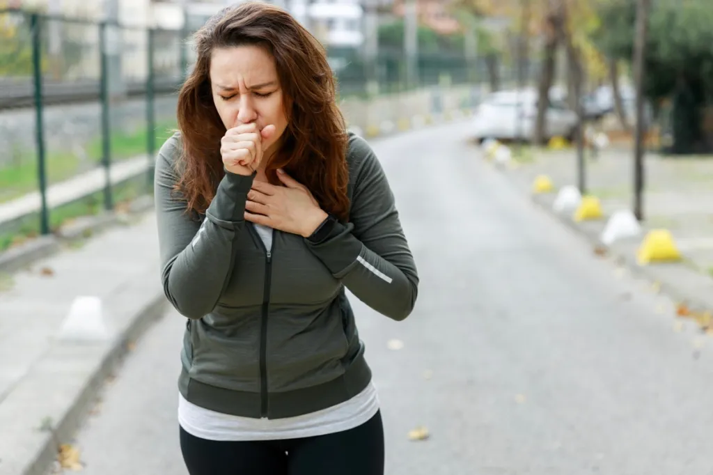 Woman in fitness wear walking on city street and coughing