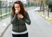 Người phụ nữ trẻ thể thao bị ho khi đi dạo trên phố.  Nữ vận động viên bị ảnh hưởng bởi ô nhiễm không khí khi tập chạy