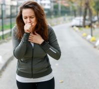 Young sporty woman coughing while walking on the street. Athlete woman affected by air pollution during running training