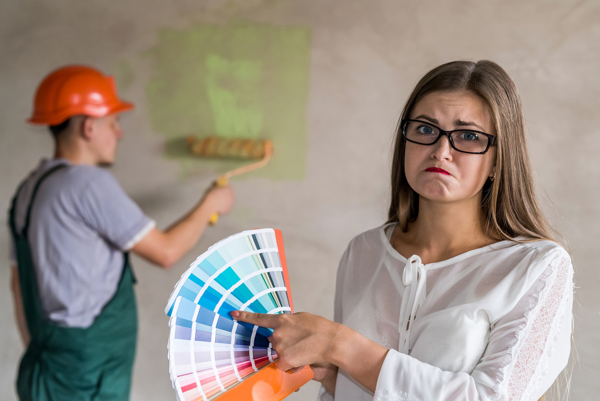 Frowning woman choosing color for painting walls in apartment