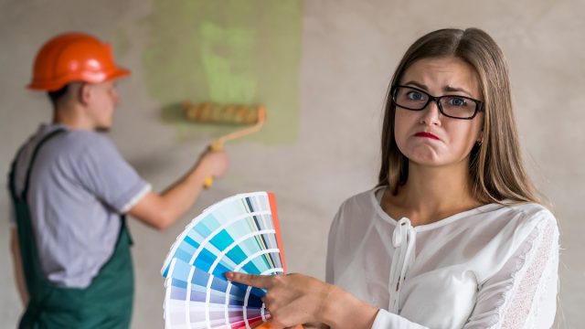 Frowning woman choosing color for painting walls in apartment