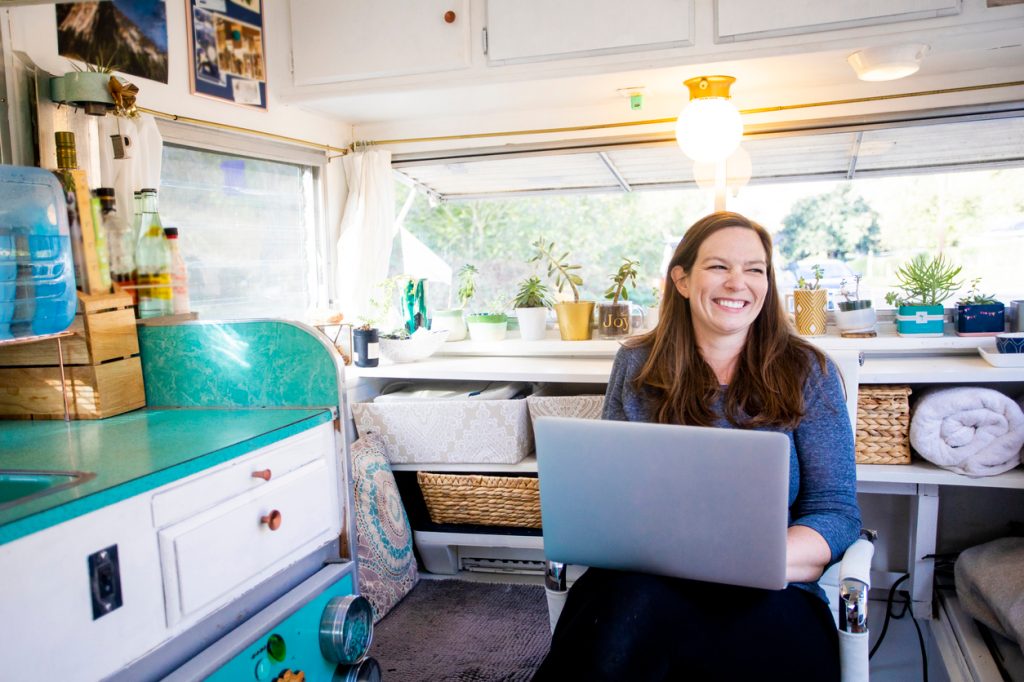 A young woman sitting on her laptop while smiling in her RV or tiny home