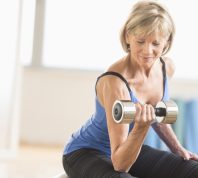 Fit mature woman lifting dumbbell while sitting at home