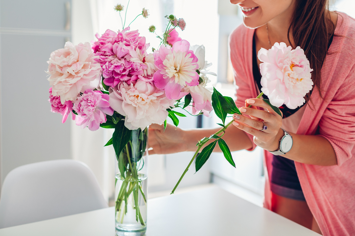 woman wearing a pink sweater puts pink peonies in a vase