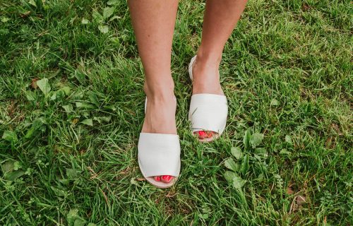 Espadrilles trắng với những ngón chân hở trên chân phụ nữ trên cỏ