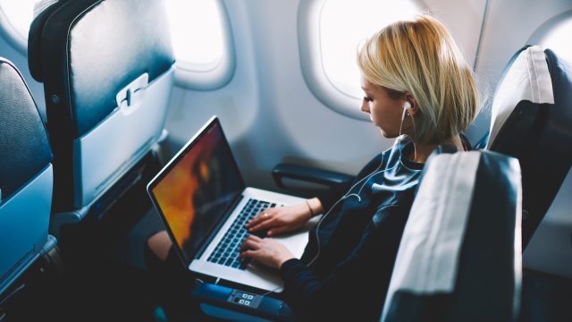 A woman working on her laptop on an airplane.
